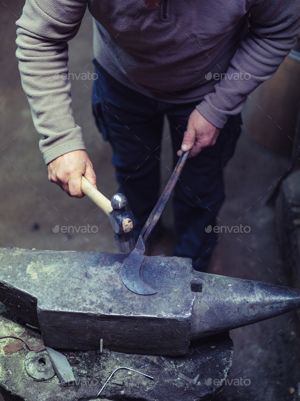 Crop anonymous master using hammer while forging metal on anvil