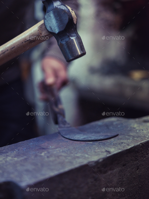 Crop man forging metal manually with hammer on anvil