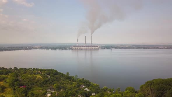 Aerial view of small village between green trees and big lake with high chimney pipes polluting alt