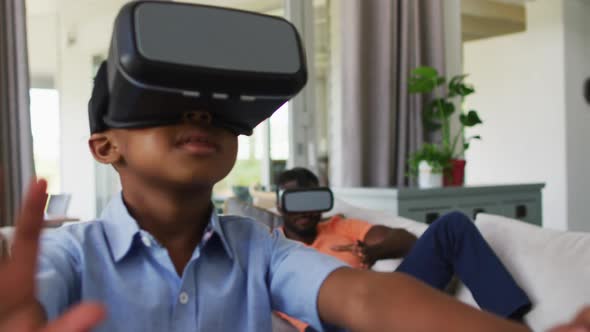 African american father and son using vr headsets together on a couch alt