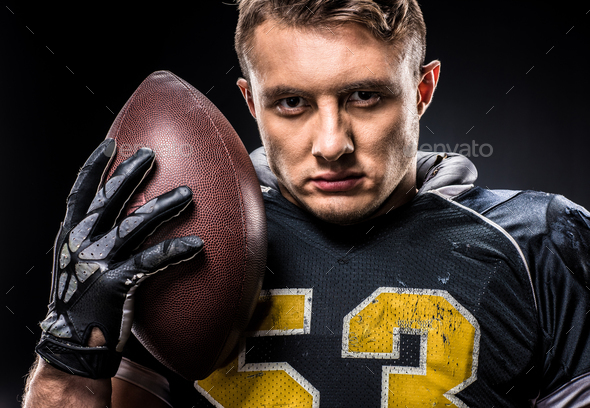 Football player with arms raised holding ball on black background