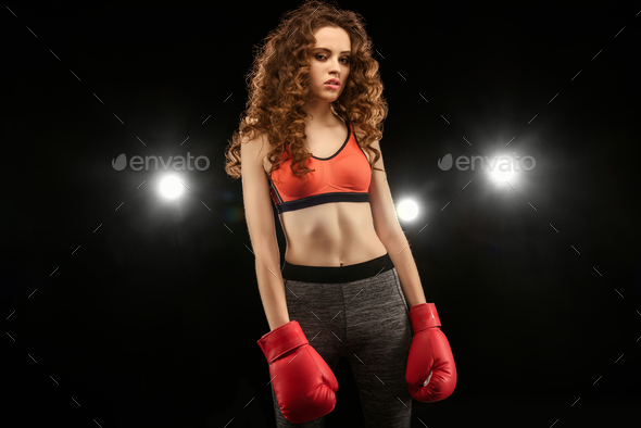 Attractive young woman boxer in red boxing gloves looking at camera