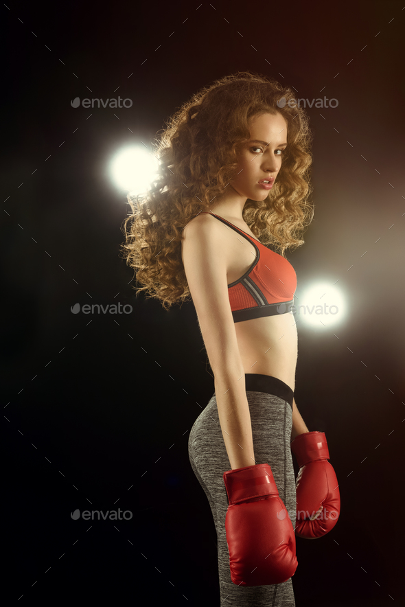 Side view of gorgeous young sportswoman in boxing gloves looking at camera