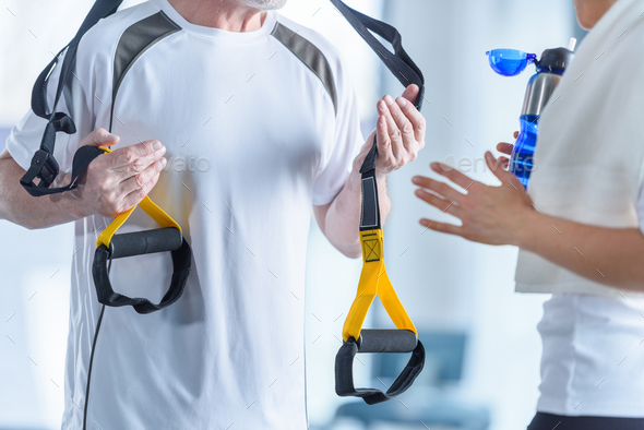 sportswoman holding sport bottle and sportsman with resistance band talking in sports center