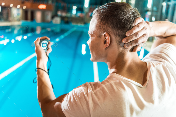 handsome swim trainer with timer standing at competition swimming pool  Stock Photo by LightFieldStudios