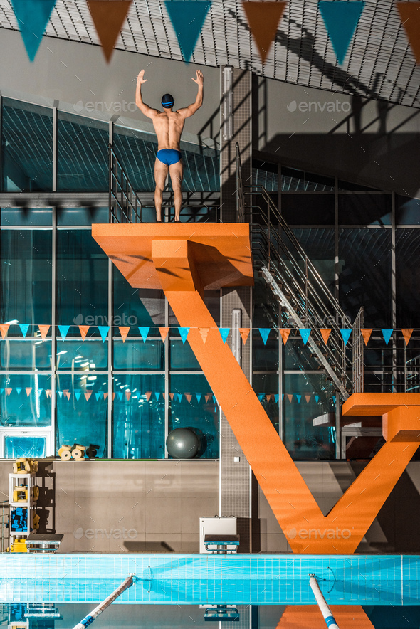 swimmer standing on diving platform ready to jump at swimming pool