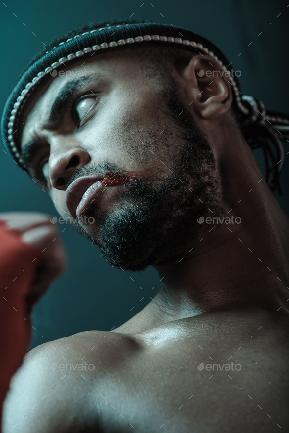 Close-up portrait of determined Muay thai fighter with blood on face looking away, ultimate fight