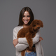 Girl holding her beloved brown toy poodle against a gray studio backdrop - PhotoDune Item for Sale