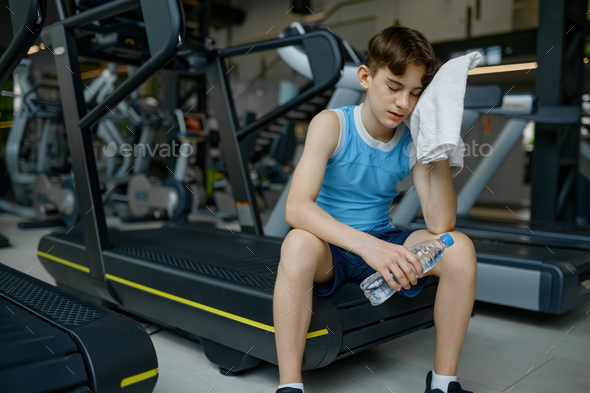 Preteen boy rest after hard training workout on treadmill at gym