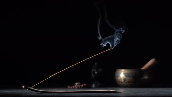 Asian incense stick in stick holder burning with smoke on black background alt