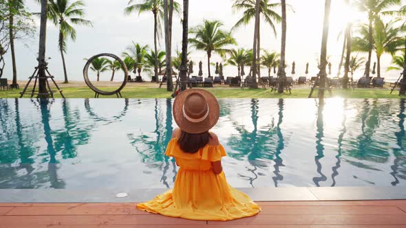 Young woman traveler relaxing and enjoying the sunset by a tropical resort pool
