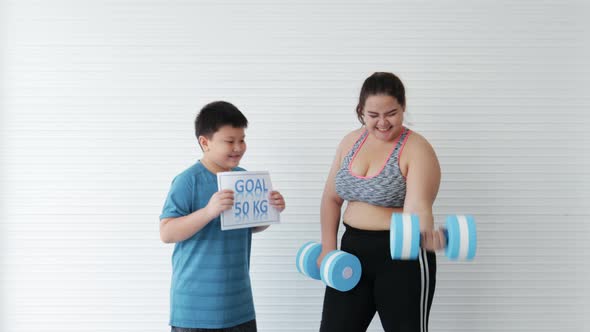 Son cheers overweight mother while lifting dumbbells for diet