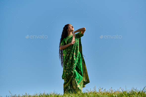 summer enjoyment, green field, indian woman in ethnic wear smiling with closed eyes under blue sky