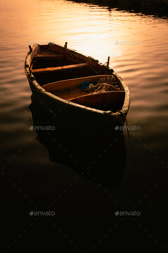Small wooden fishing boat moored with glow of light at dawn Stock