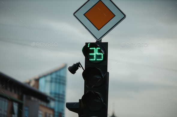 Green traffic light for cars and the main road sign; 3 seconds left