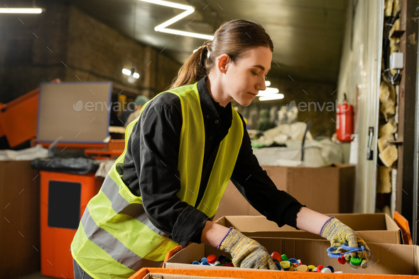 Young female worker of garbage sorting center wearing protective clothing and gloves while working