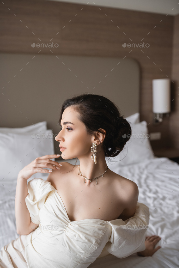 side view of enchanting young bride in white dress and luxurious jewelry  with pearl earrings Stock Photo by LightFieldStudios