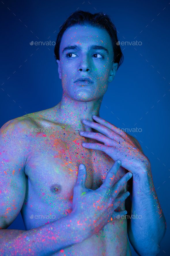 young, shirtless and eye-catching man posing in vibrant colorful neon body  paint, touching bare Stock Photo by LightFieldStudios