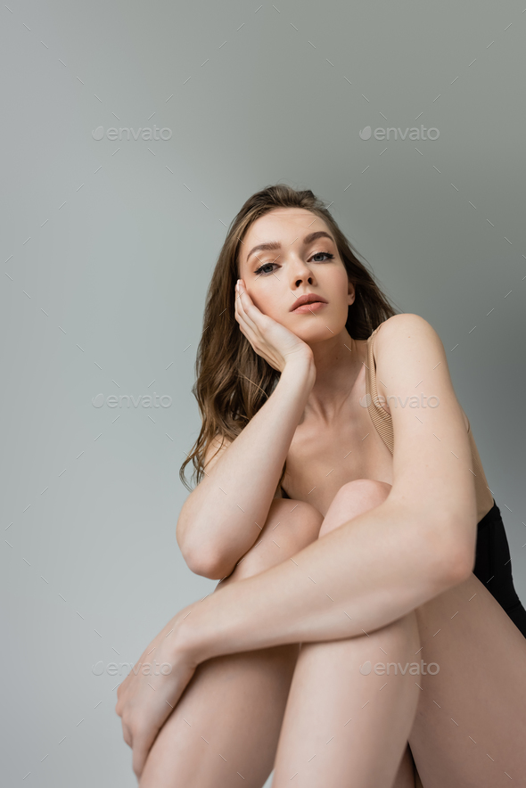 Portrait of stylish young woman in natural makeup and hairstyle looking at camera and hugging knee