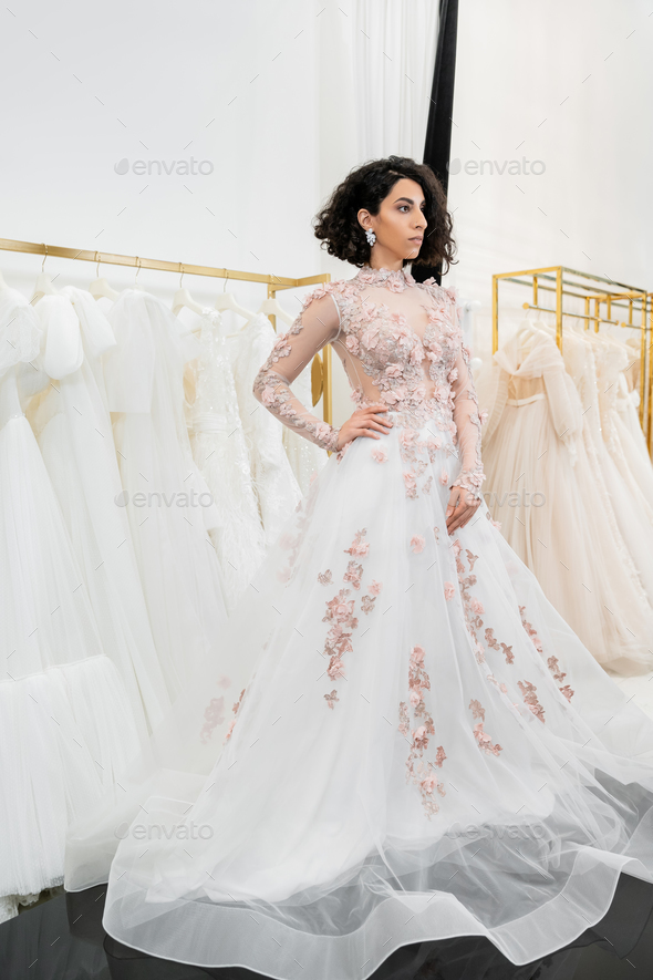 brunette and middle eastern woman with wavy hair trying on gorgeous and floral wedding dress