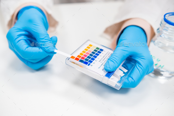 Close up scientist test checks a pH using indicator paper