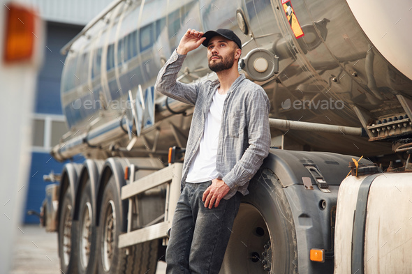 Touching the black cap. Young truck driver in casual clothes