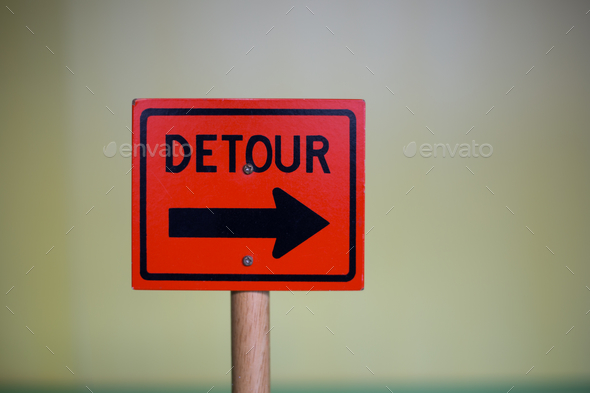 Closeup shot of a red Detour sign with a black arrow indicating the direction