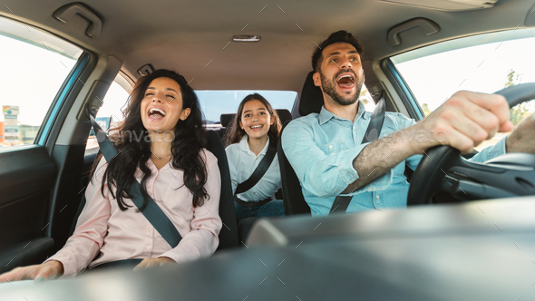 Excited european family of three riding car and singing, parents and daughter enjoying auto ride