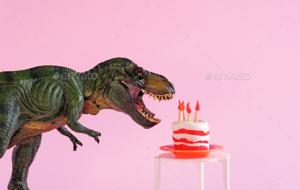 Cute dinosaur toy with birthday cake on table on pink background.