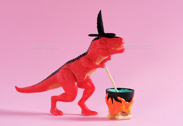 Red dinosaur wearing witch hat is brewing potion in pot on pink background. Halloween greeting card.