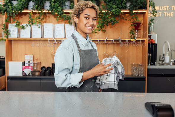 Smiling female bartender wiping glass with towel. Woman barista at
