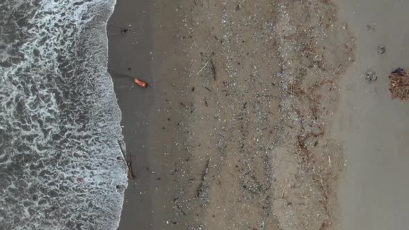 Ascending, rising drone shot of a badly polluted beach, tons of plastic and a men piling up garbage alt