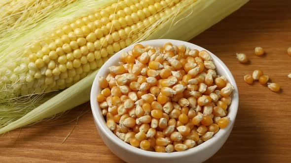 Fresh raw corn on the cob and a bowl with dried seeds  alt