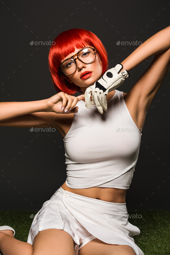 seductive young woman with red bob cut in golf glove and stylish eyeglasses looking at camera on