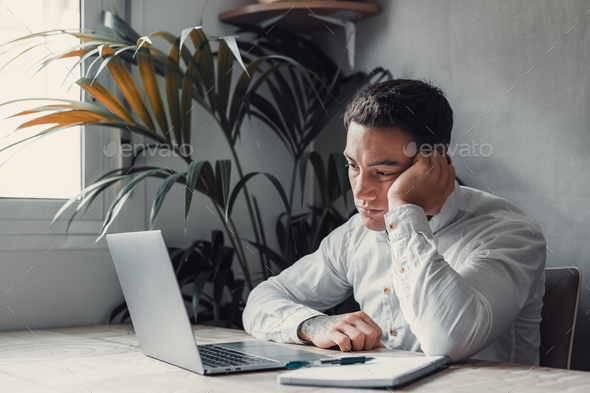 Tired male student or worker sit at home office desk look in distance having sleep