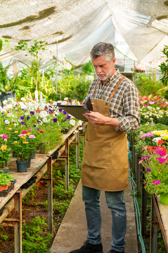 Seasoned Nursery Worker Capturing Vibrant Flora, Jotting Customer Requests