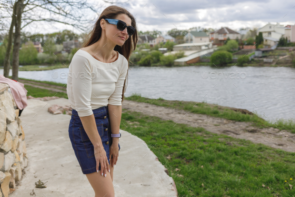 Young woman in short denim skirt and blouse walking along the lake