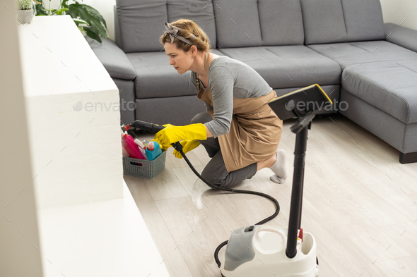 The woman washes the floor in the room with a white steam cleaner, a wet high-pressure steam