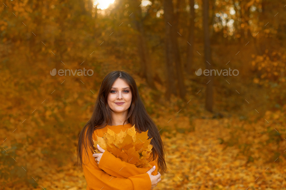 woman hugs self, care about mental health, holding leaves bouquet and walking in autumn park