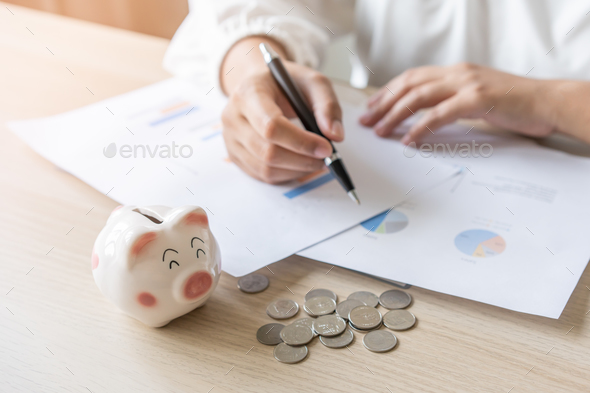 Woman save money for business investment with graph summary profit report. Selective focus at pig.