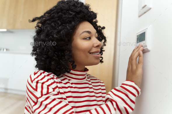 Portrait of handsome smiling African American standing in apartment using smart home control pane