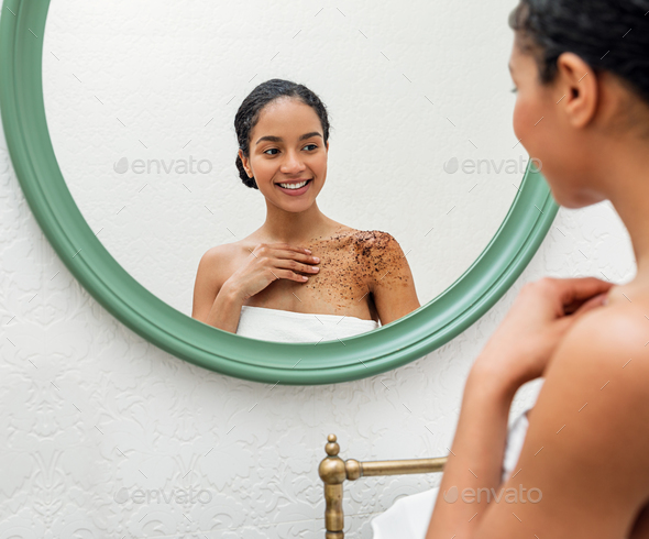 Smiling woman applying coffee bean body scrub in bathroom