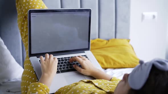 Woman in Yellow Pajamas Works on Laptop in Bed