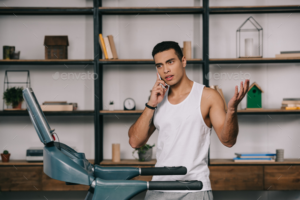 bi-racial sportsman talking on smartphone near treadmill