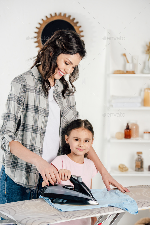 mother in grey shirt and daughter ironing at home