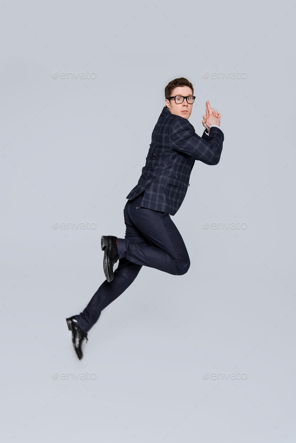 stylish businessman jumping with hand gun gesture isolated on grey