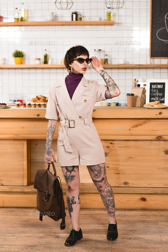 fashionable, tattooed businesswoman in sunglasses standing at bar counter in cafeteria