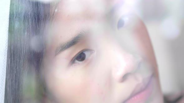 Close up Asian woman face sitting beside a window and looking through out the window alt