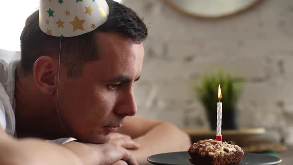 Thoughtful Sad Man Sitting in Front of Little Cake with Lighted Candle.