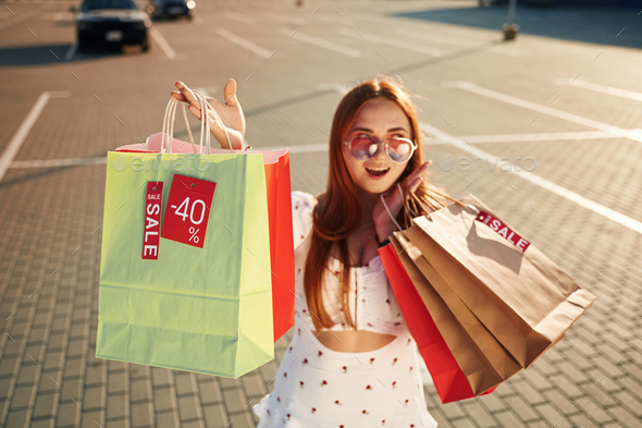 Crazy sales sticker. Beautiful woman in casual clothes is holding shopping bags, outdoors